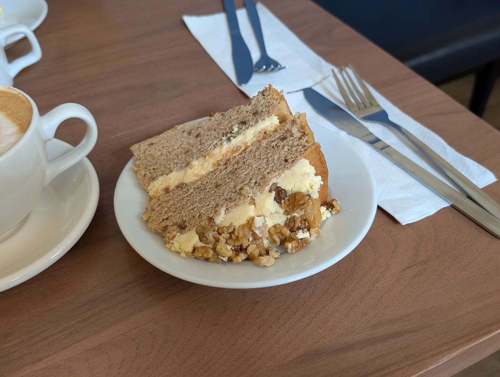 Ein Stück Schichtkuchen und ein Cappuccino auf einem Holztisch